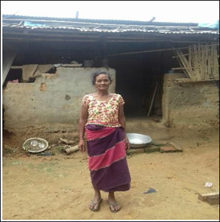 A rural woman standing outside her old kutcha mud house before receiving support under PMAY-G.