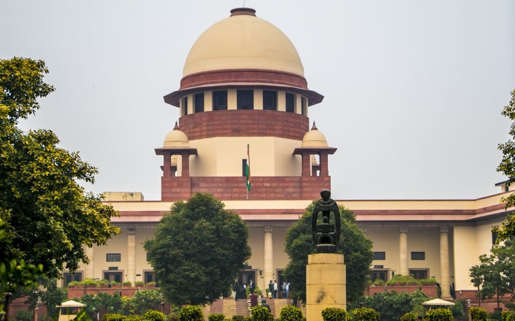 Front view of the Supreme Court of India building in New Delhi, designed by architect Ganesh Bhikaji Deolalikar in 1958, featuring its central dome and statue of justice.