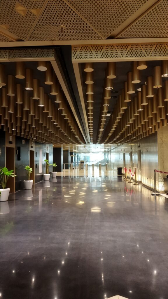 Modern interior corridor at Yashobhoomi with reflective flooring, gold-toned ceiling panels, and ambient lighting.
