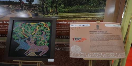 A framed tribal art painting displayed alongside an information panel at the Tribal Business Conclave 2025 exhibition.