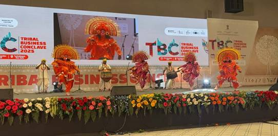 Tribal artists performing a vibrant traditional dance in ornate orange headgear and costumes at the Tribal Business Conclave 2025.