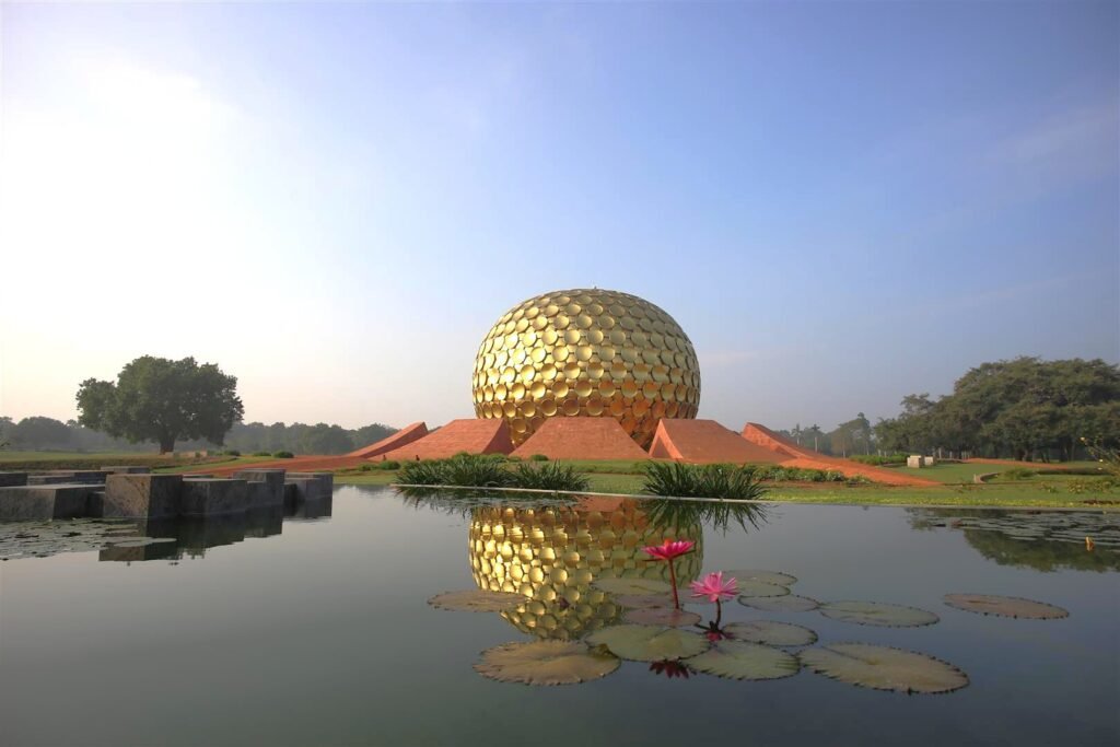 Golden spherical Matrimandir structure in Auroville reflected in a lotus pond during sunrise, surrounded by lush green landscape.