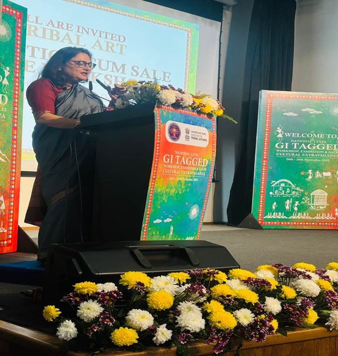 Nests A speaker addresses the audience from a decorated podium during the National Level GI-Tagged Tribal Art Workshop & Exhibition – Cultural Extravaganza at IGNCA, New Delhi, with vibrant floral arrangements and event banners in the background.