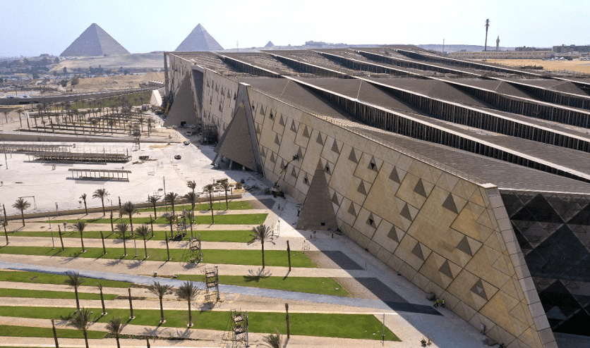 Aerial view of the Grand Egyptian Museum showcasing its triangular façade with the Giza Pyramids visible in the background.