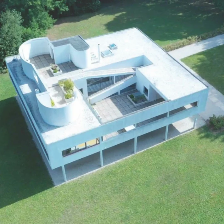 Aerial view of Villa Savoye in Poissy, France, showing its modernist white form, roof terrace, curved volumes, and pilotis supporting the structure.