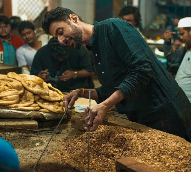A chef Ranveer preparing traditional Awadhi cuisine in a busy Lucknow kitchen, surrounded by freshly baked sheermal bread and spices.