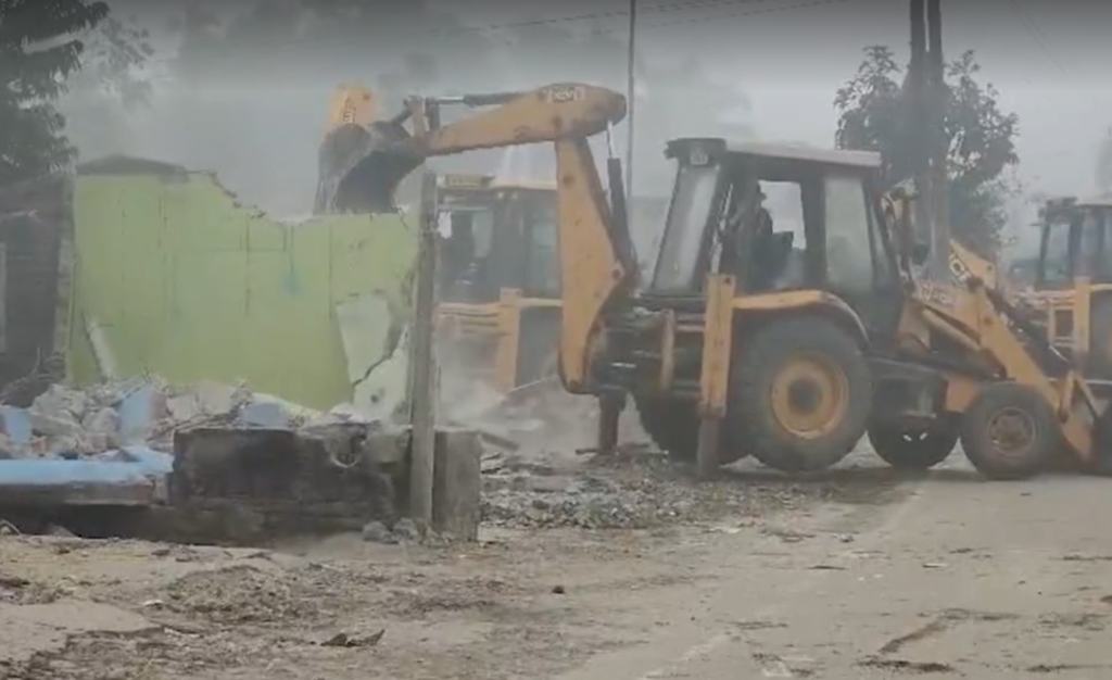 Heavy earthmoving machinery demolishing roadside structures during infrastructure expansion work in Assam