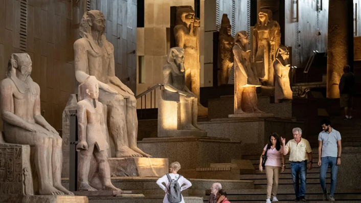 Visitors walking along the Grand Staircase of the museum, surrounded by monumental statues from different Egyptian dynasties.