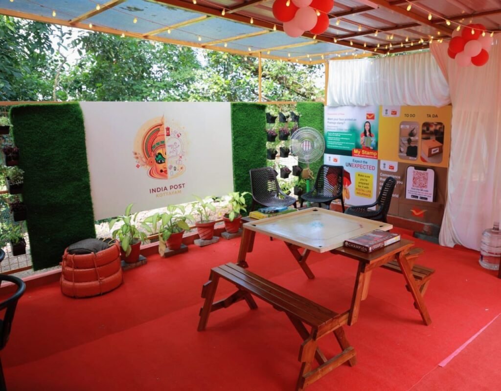 Outdoor café-style seating area at the Gen-Z Post Office Extension Counter, featuring colourful wall art, refurbished tyre seating, and a vertical garden.