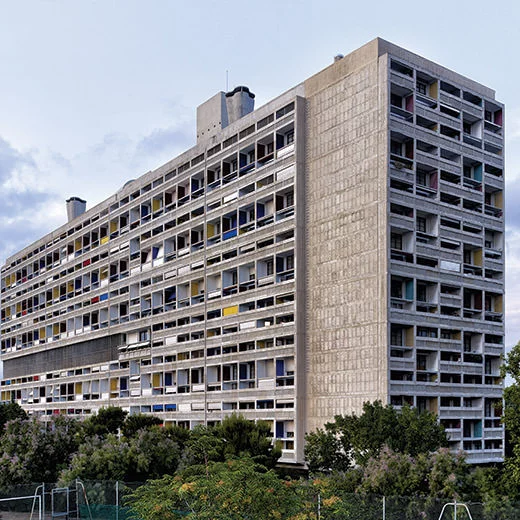 Exterior view of the Unité d’Habitation showing its tall concrete block structure with modular housing units and colorful balcony recesses.