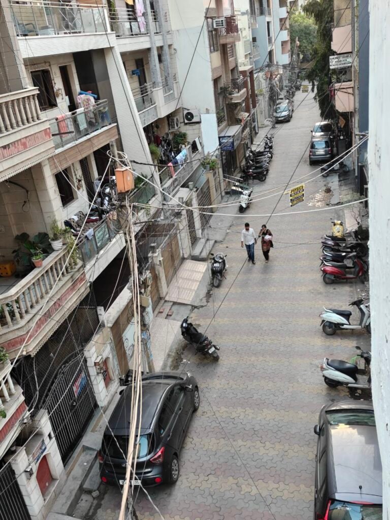 Narrow residential lane in Delhi dominated by parked cars and scooters
