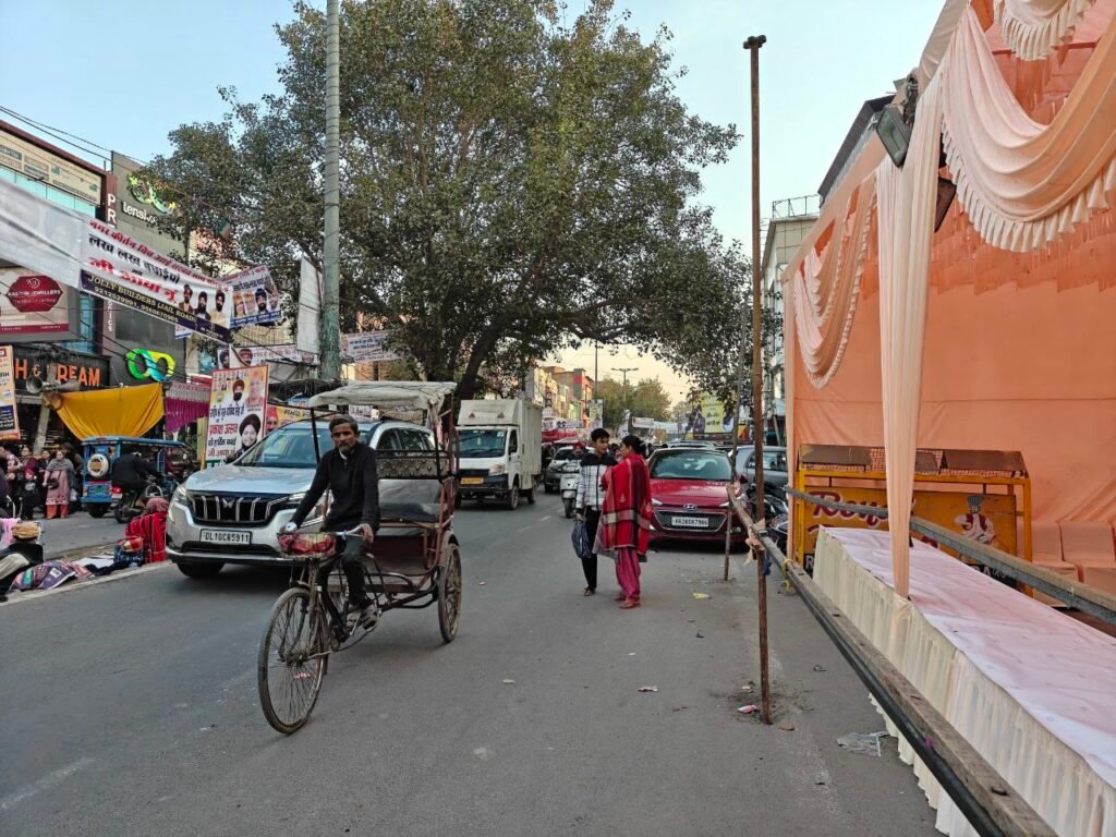 E-rickshaw, pedestrians, and vehicles sharing road space during a temporary street setup on Jail Road in West Delhi