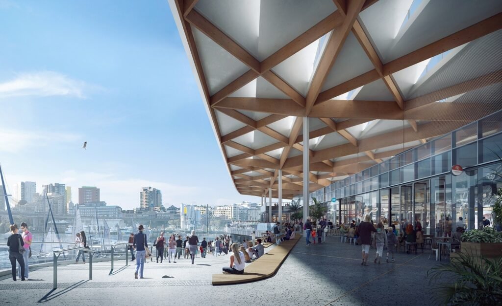 Waterfront promenade at the Sydney Fish Market featuring stepped seating, glass façades, and the floating timber canopy roof overlooking Blackwattle Bay.