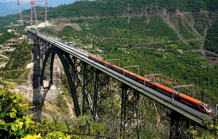 Vande Bharat Express train running on a steel arch railway bridge through green mountainous landscape in India