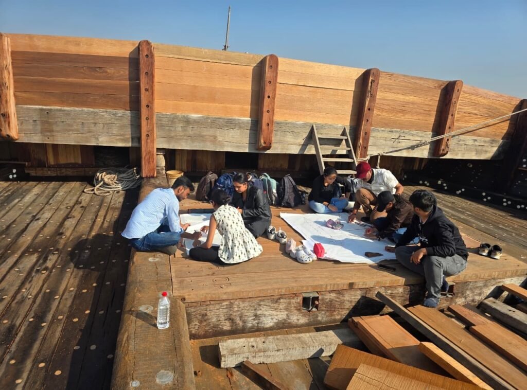 Architecture students sketching and documenting wooden boat structure on site in Mandvi
