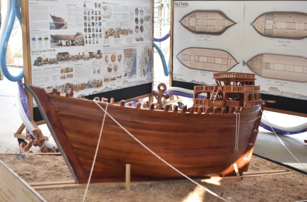 Wooden boat model with architectural panels displaying Mandvi shipbuilding study