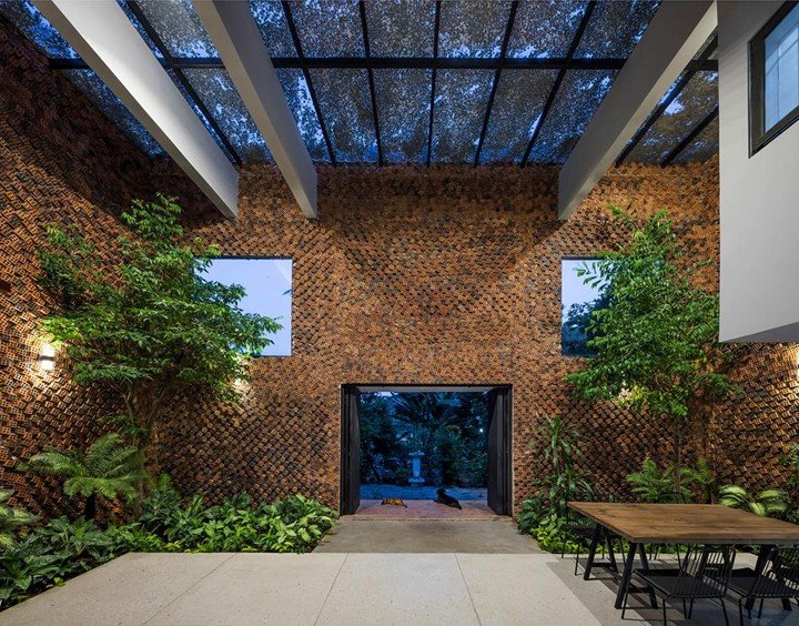 Contemporary courtyard space with textured brick walls, indoor greenery, and skylight roof in sustainable architecture project