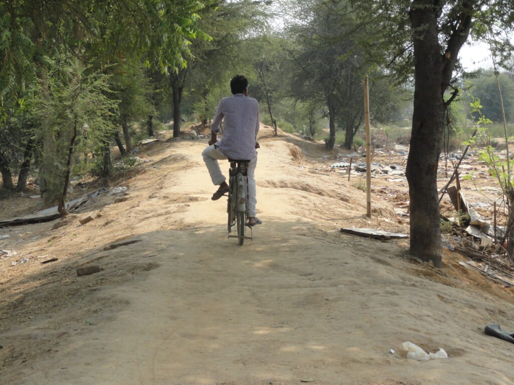 Cyclist navigating the deteriorated Bundh pathway before the Gurugram urban regeneration project.
